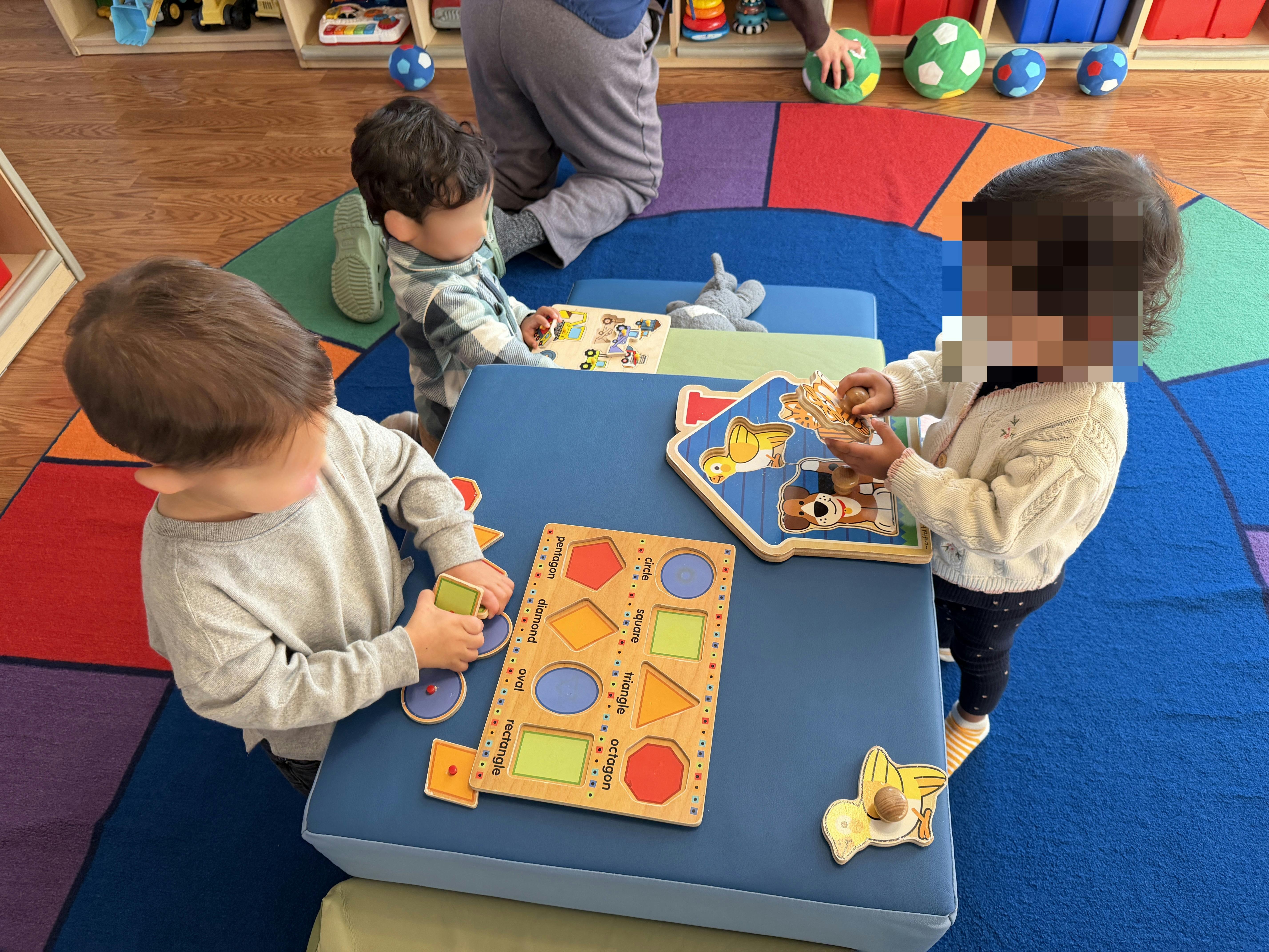 Three children playing with puzzles on a blue table in a classroom