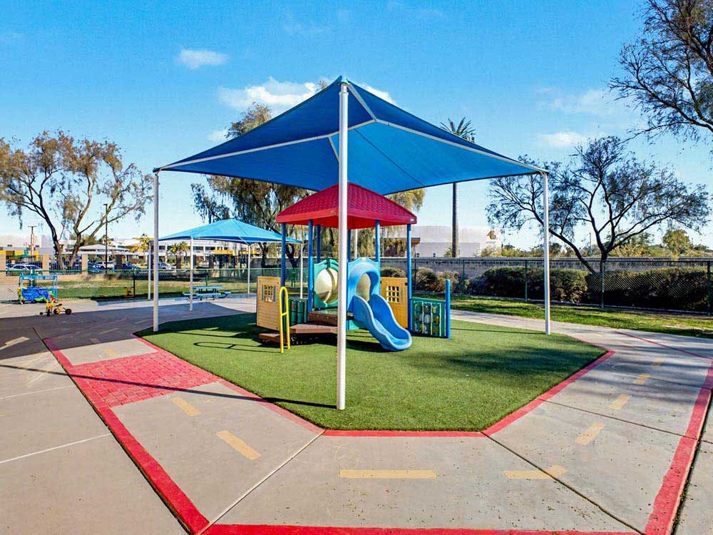 Playground with blue canopy, slides, and tricycles on a paved path