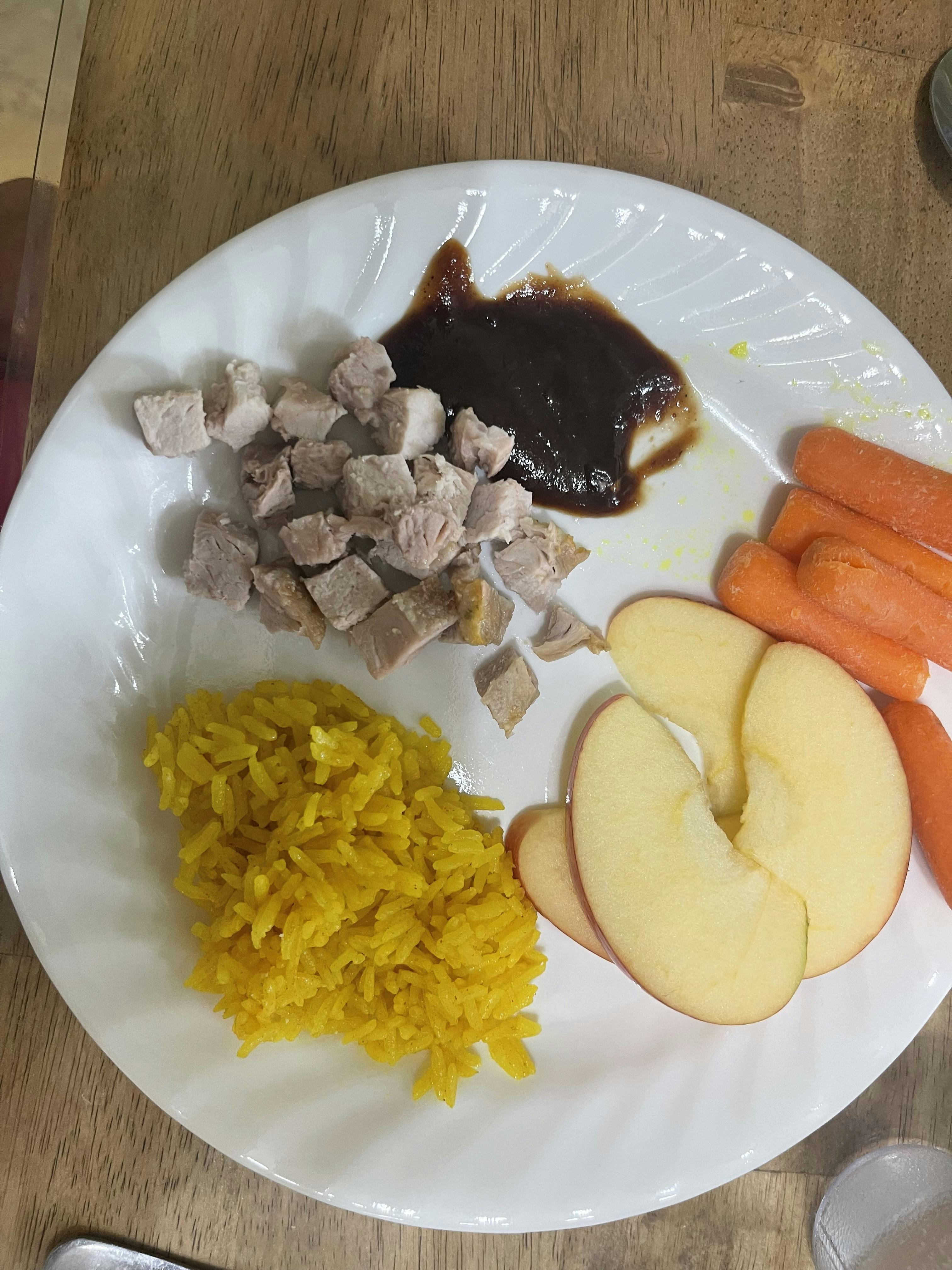 Plate of diced meat, sauce, yellow rice, apple slices, and carrots