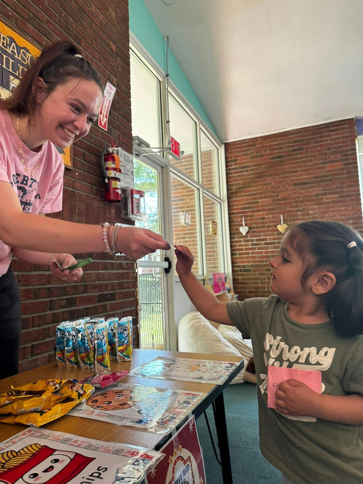 Person exchanging items with a child at a table with snacks