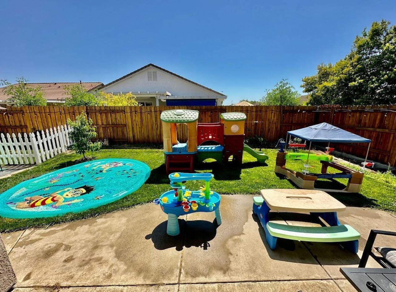 Backyard with children's play structures, water mat, and picnic table