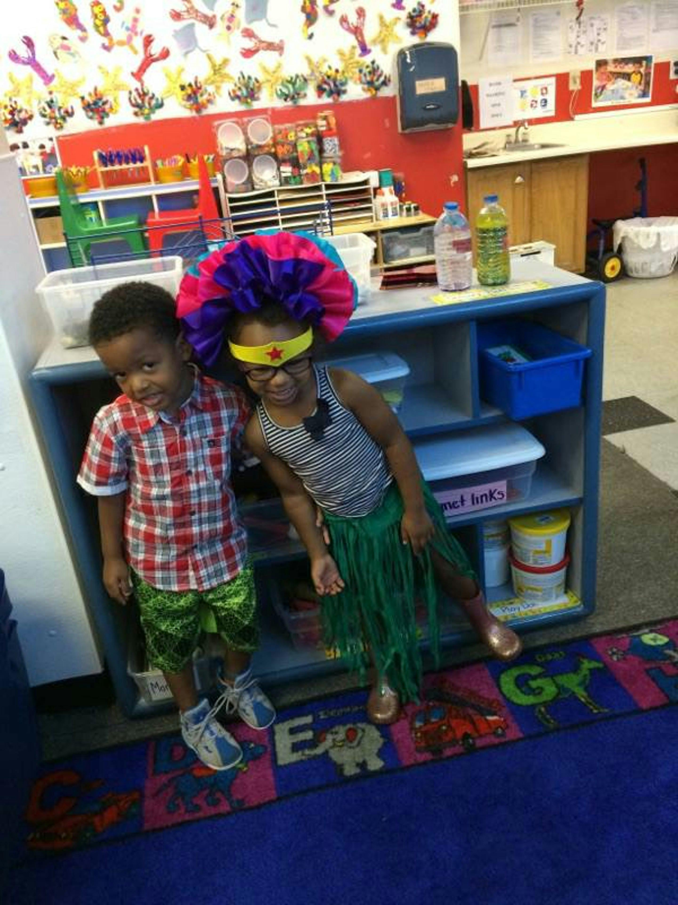 Two children in costumes standing next to a shelf in a classroom
