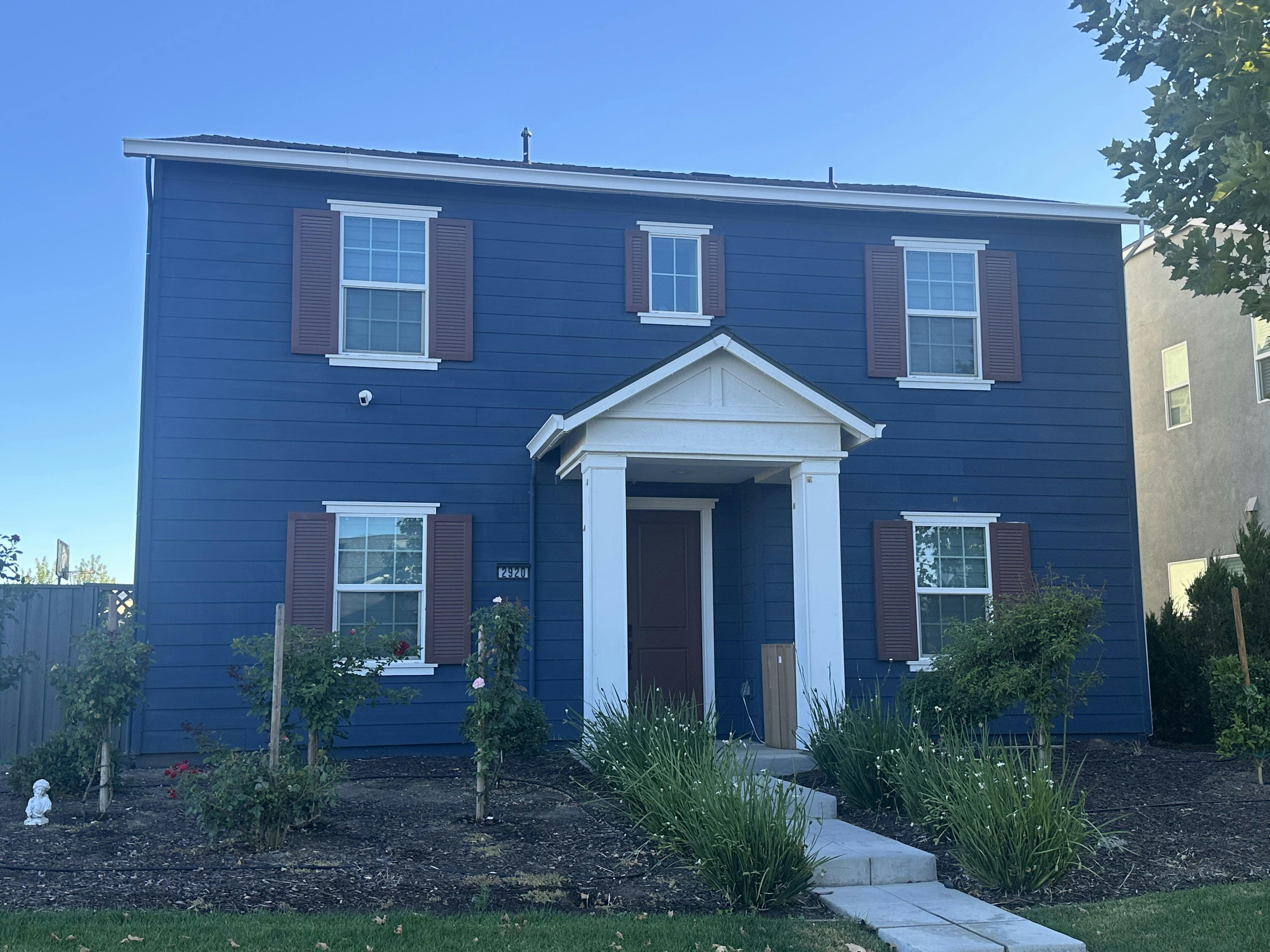 Two-story blue house with brown shutters and a white front porch