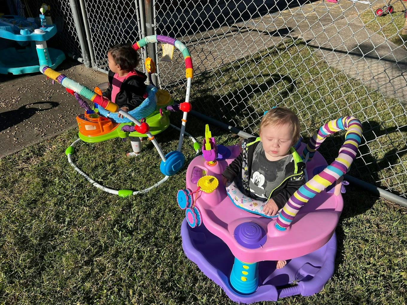 Two children in baby activity centers on grass