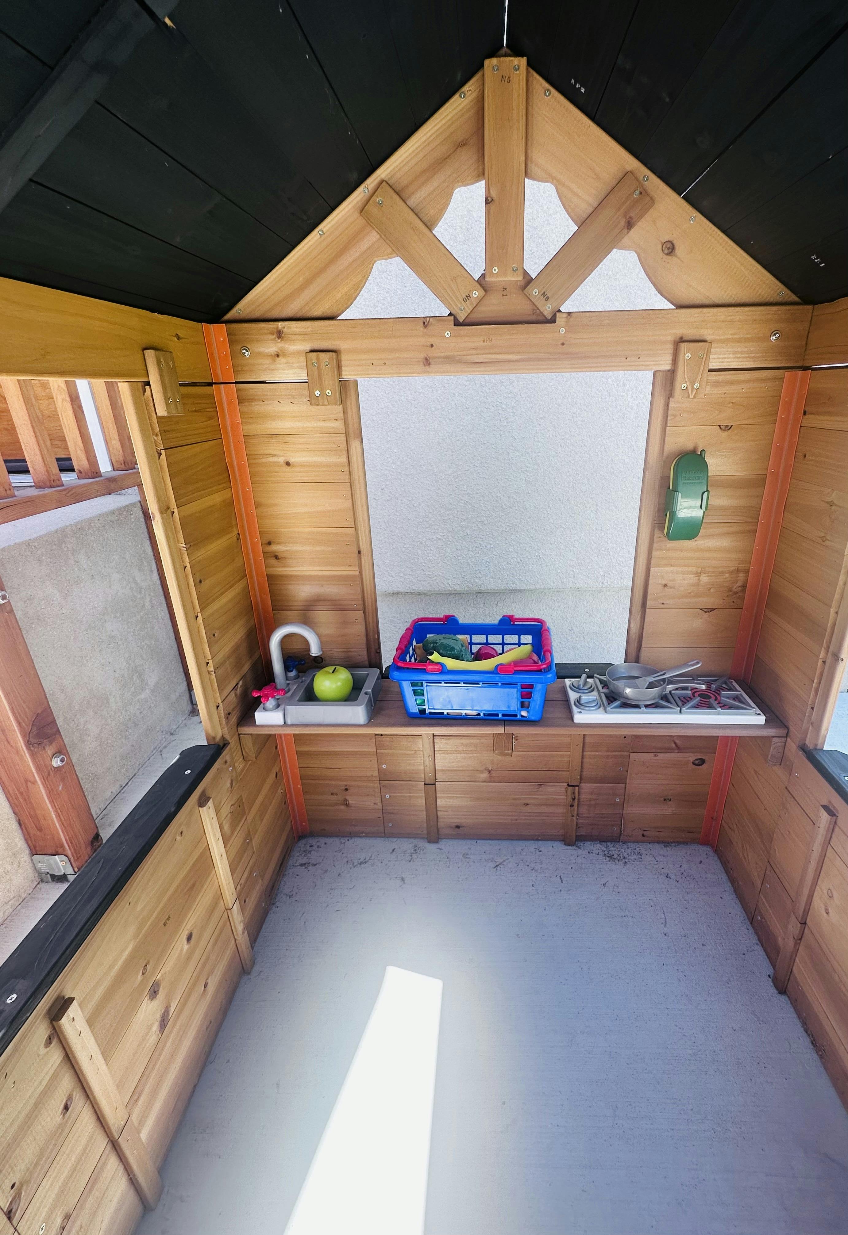 Wooden play kitchen with a toy sink, stove, and basket of plastic food
