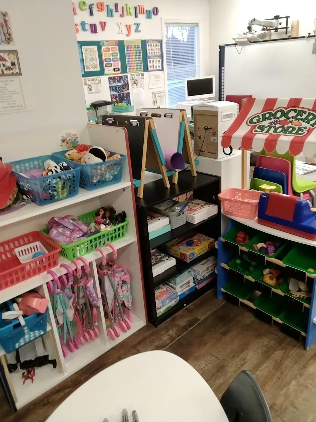 Classroom with shelves of toys, a small grocery store play set, and an easel