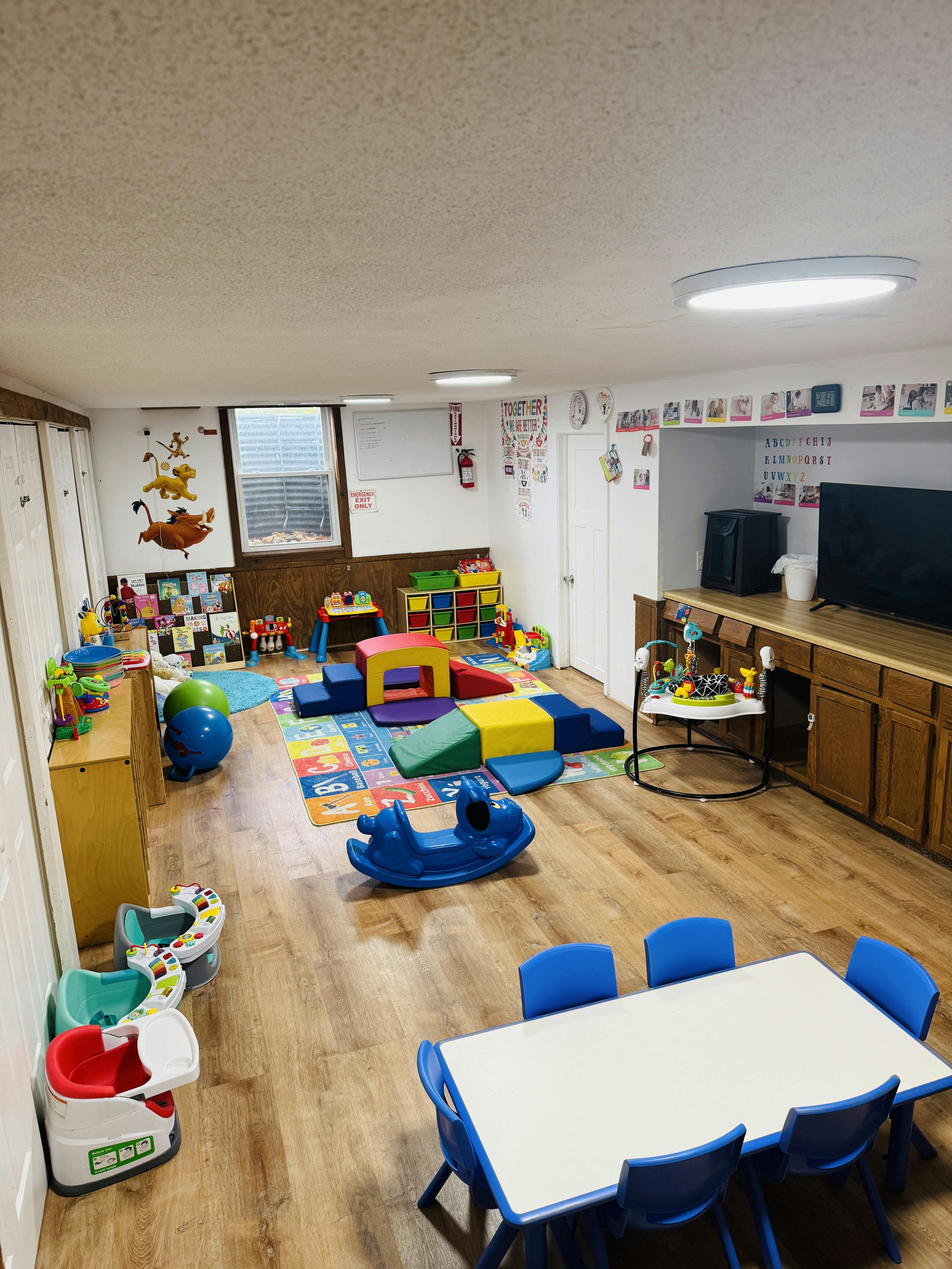 Childcare playroom with colorful mats, soft play structures, and small tables with chairs