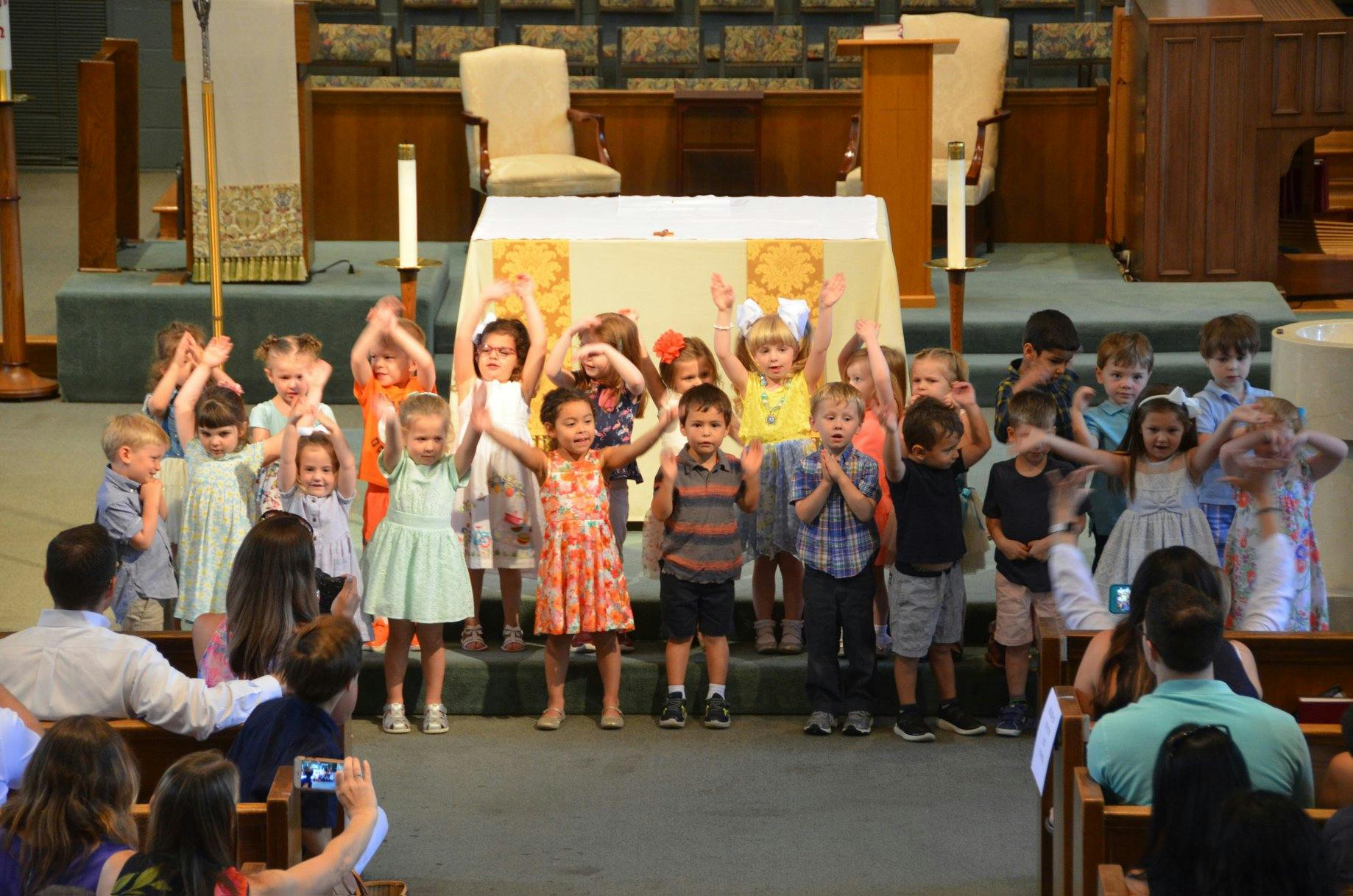 Group of children standing with hands raised in front of seated adults