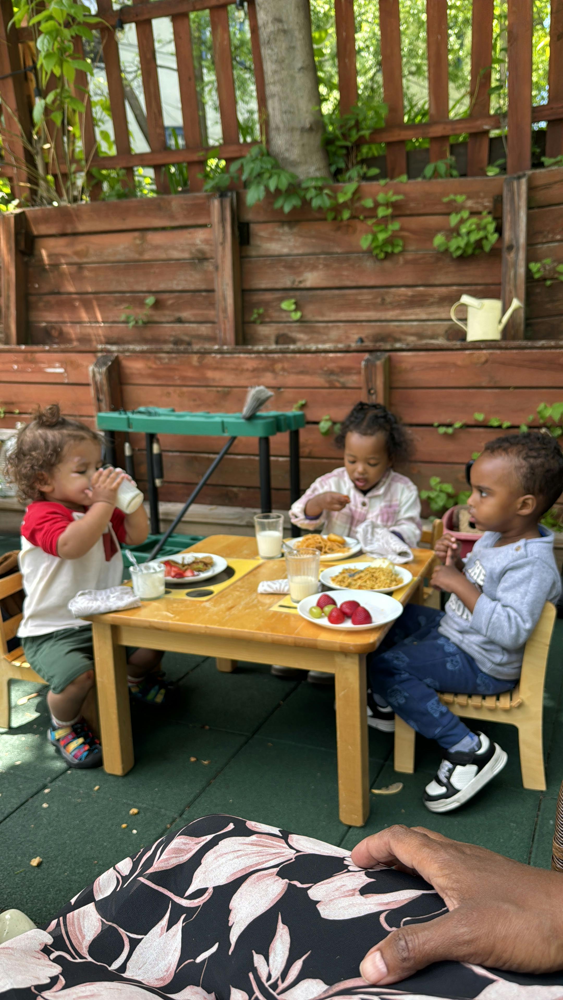 Three children sitting at a table with plates of food and drinks