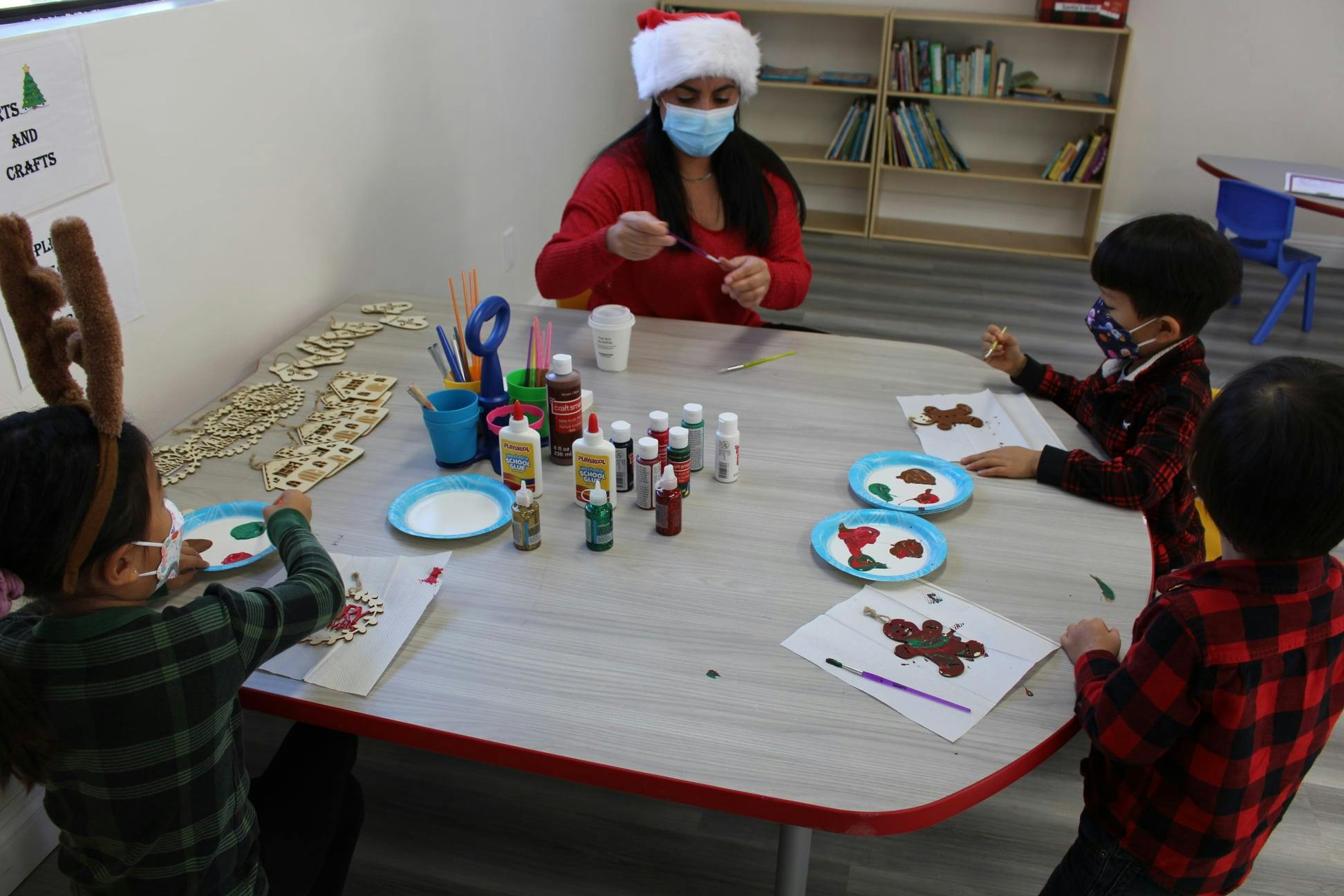 Adult in Santa hat and mask with three children doing crafts at a table