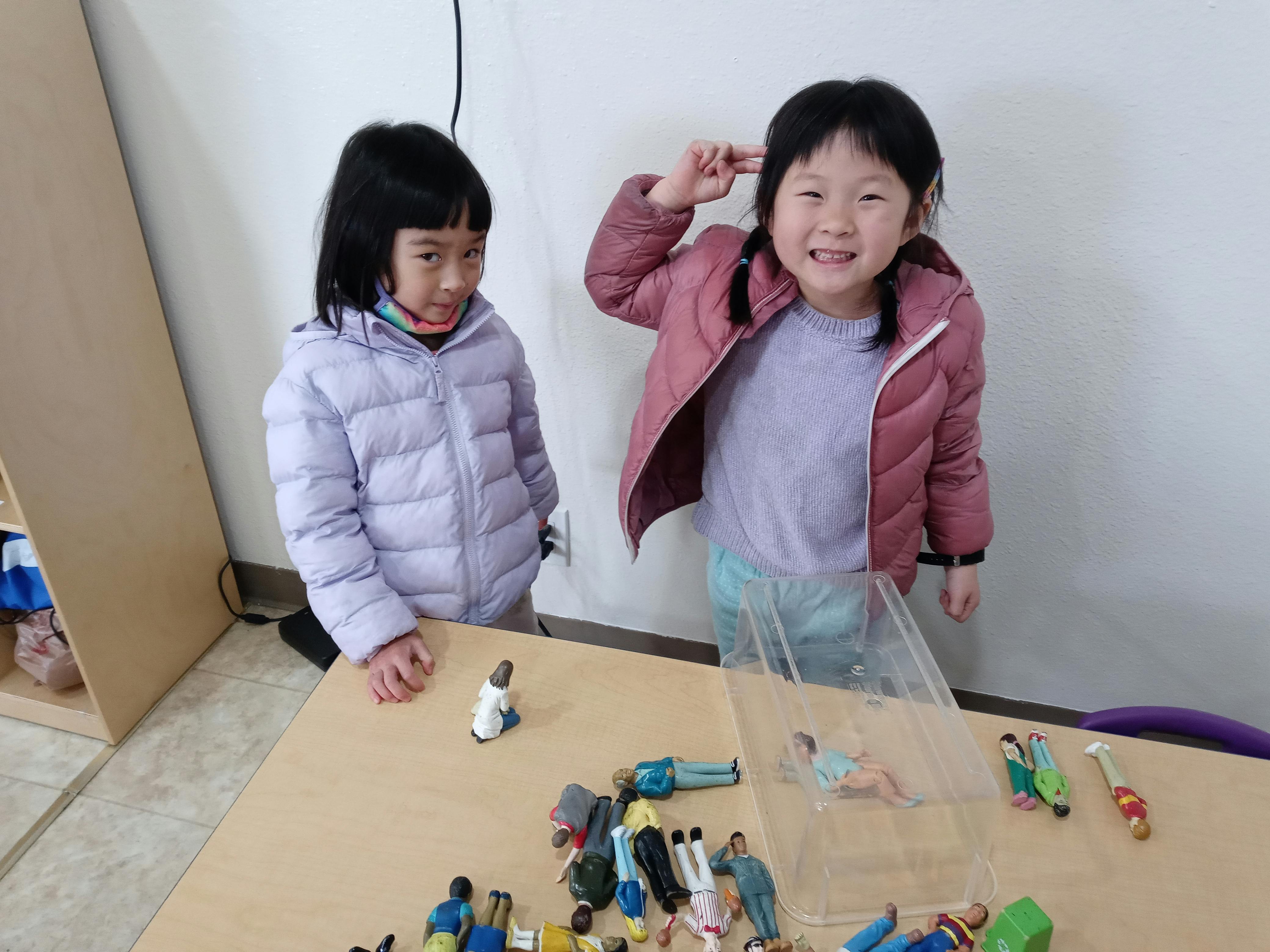 Two children standing at a table with small figures