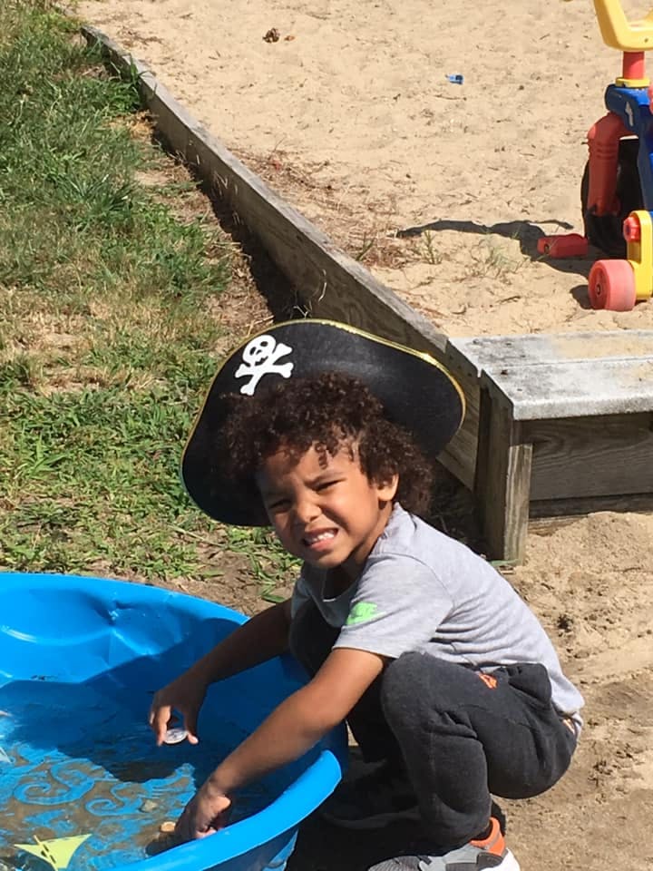 Child in a pirate hat playing in a blue plastic pool