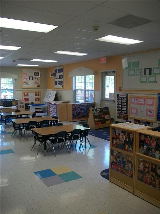Empty classroom with small tables and chairs, whiteboards, and children's artwork