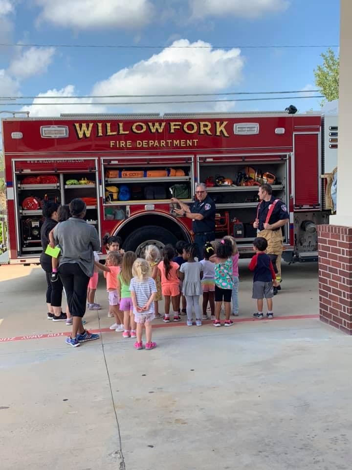 Firefighters showing equipment on a fire truck to a group of children