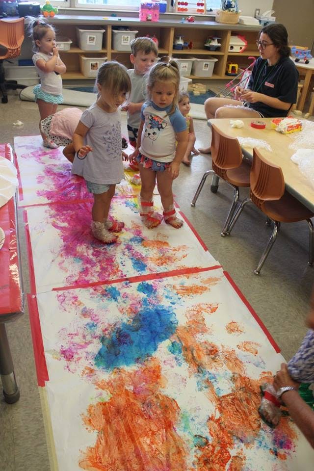 Children standing on a large paper with colorful paint footprints