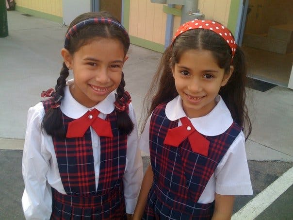 Two children in school uniforms with plaid dresses and red bows
