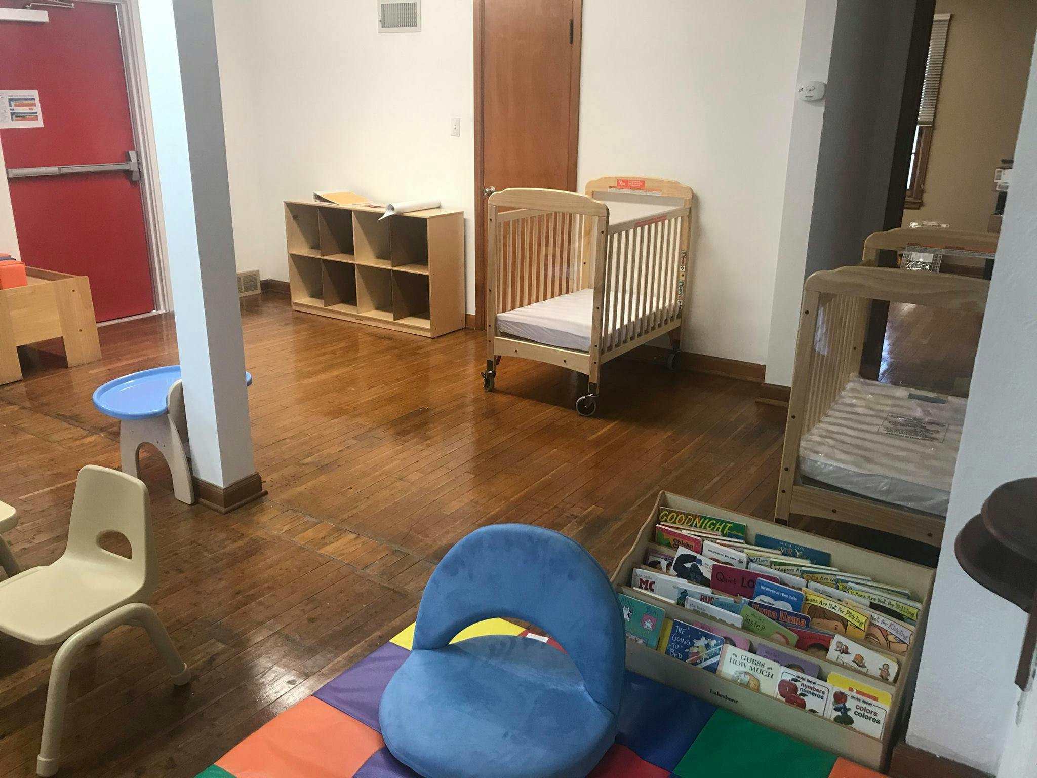 Room with cribs, child-sized chairs, and a bookshelf