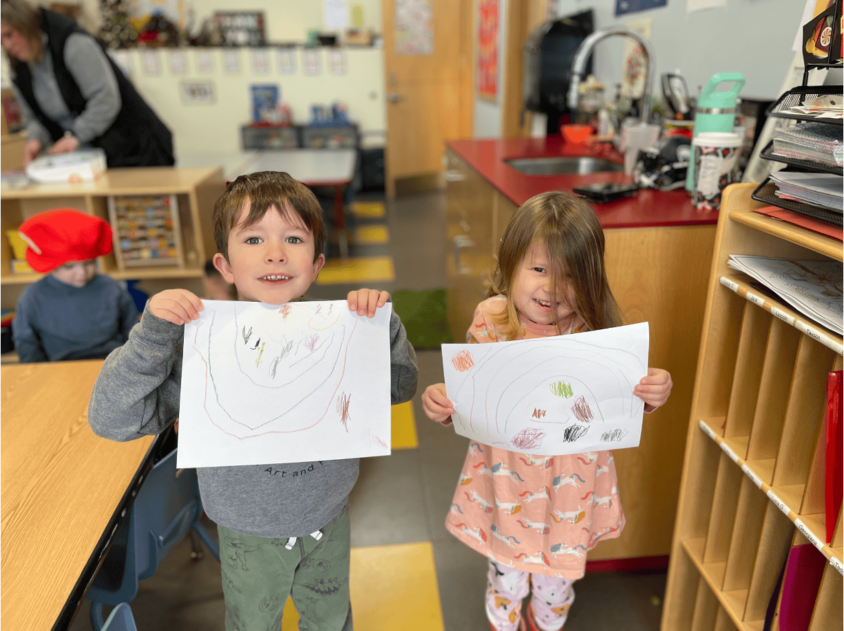 Two children holding up their drawings in a classroom