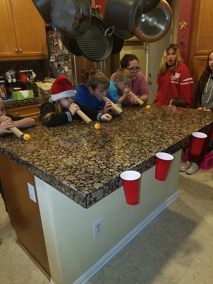 People playing a game with tubes and small balls on a kitchen island