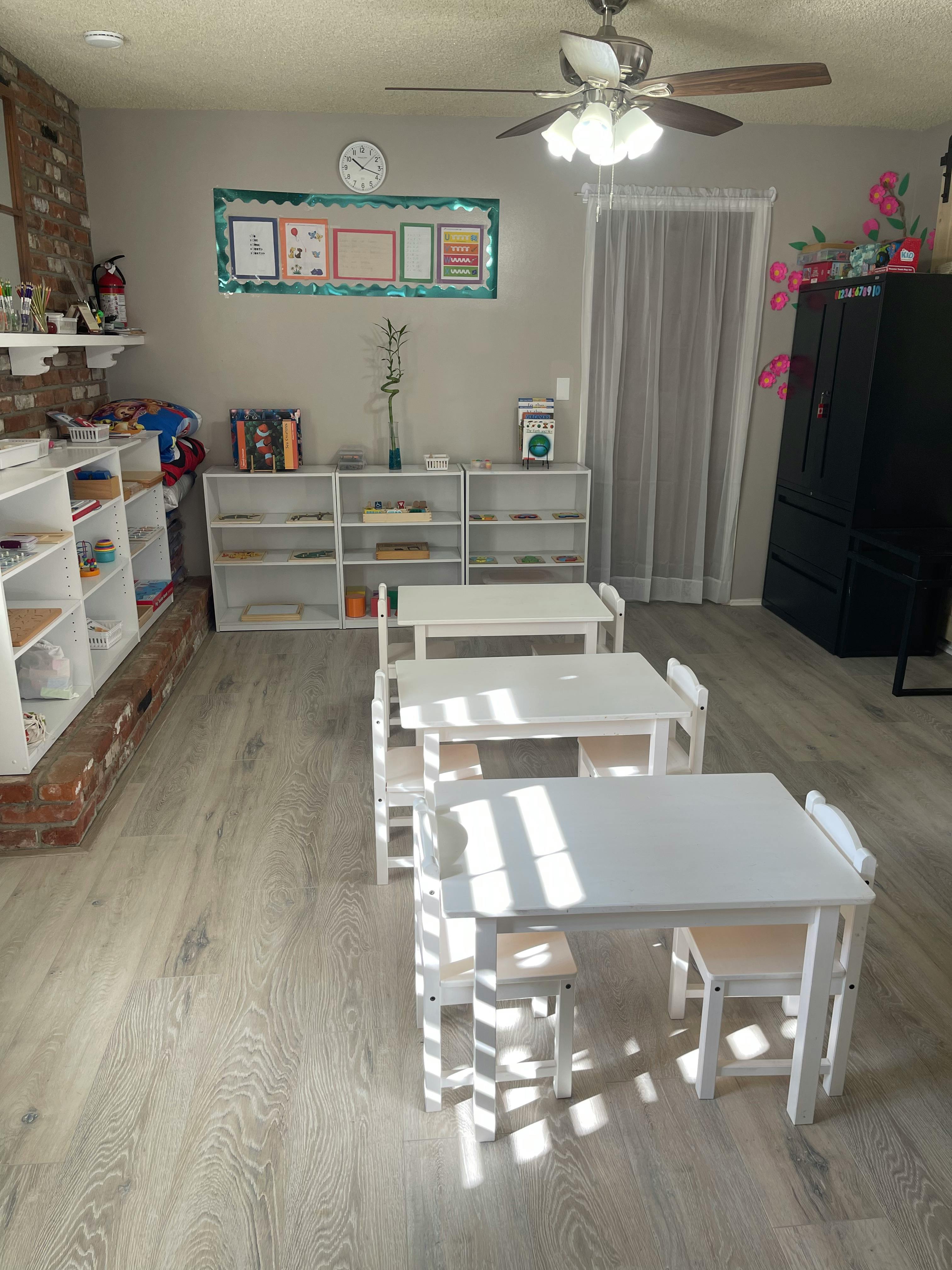 Classroom with small white tables and chairs, shelves, and a ceiling fan