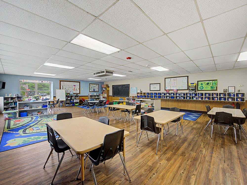 Classroom with small tables and chairs, storage units, and a learning rug