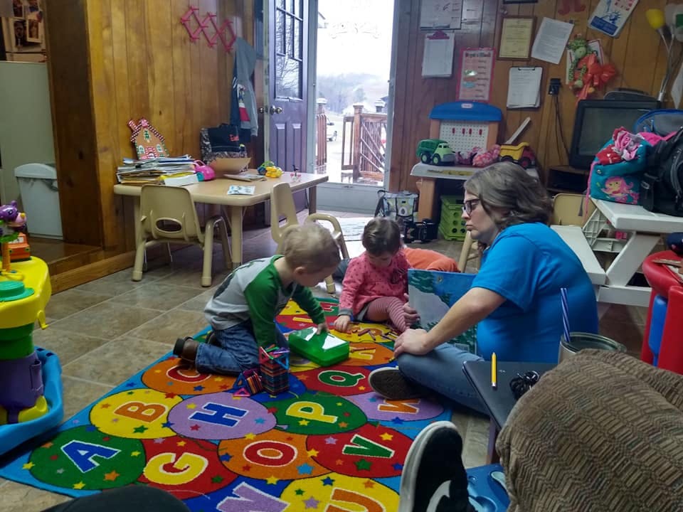 Person and two children playing on an alphabet rug