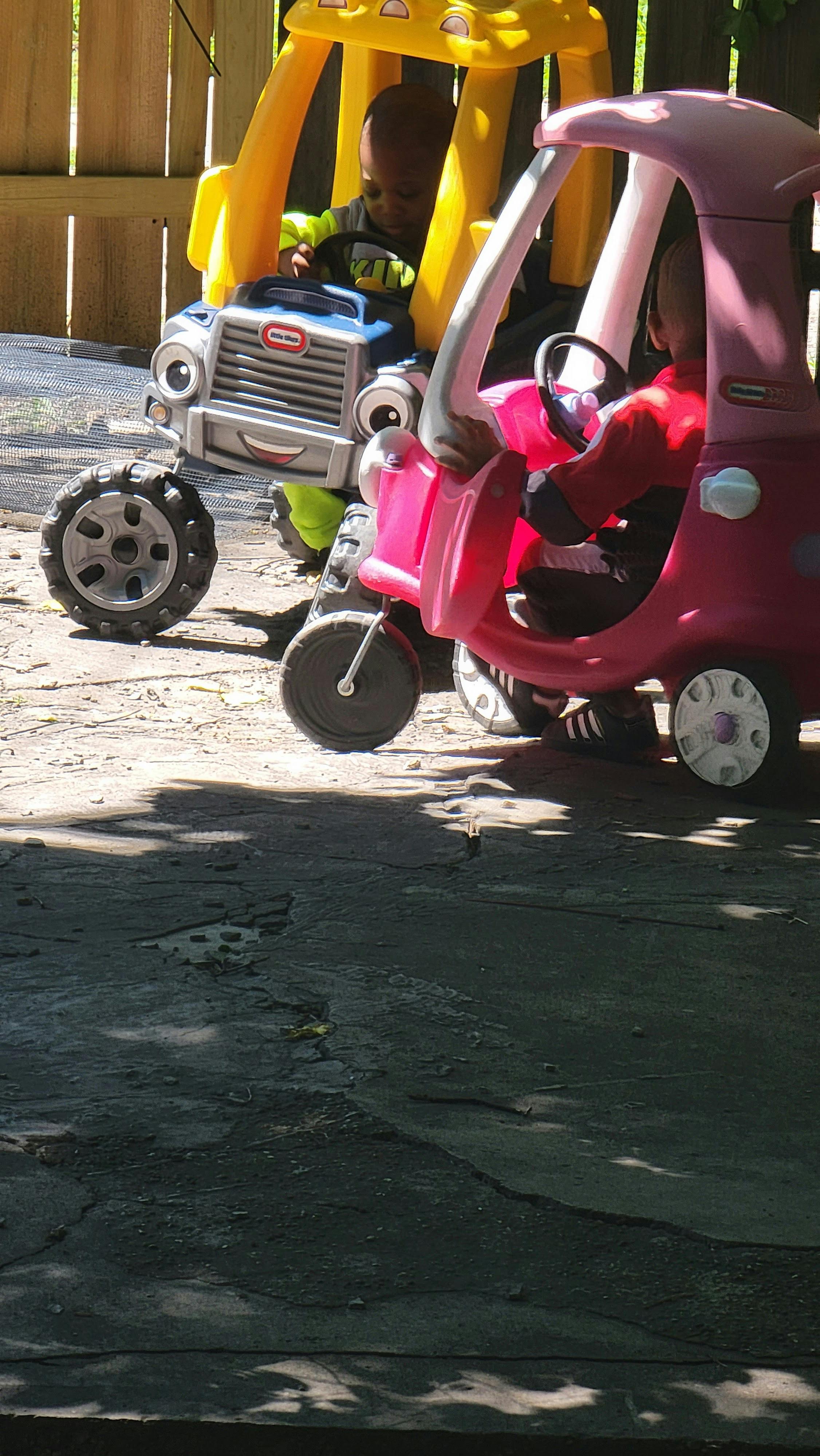 Two children in toy cars, ride-on cars