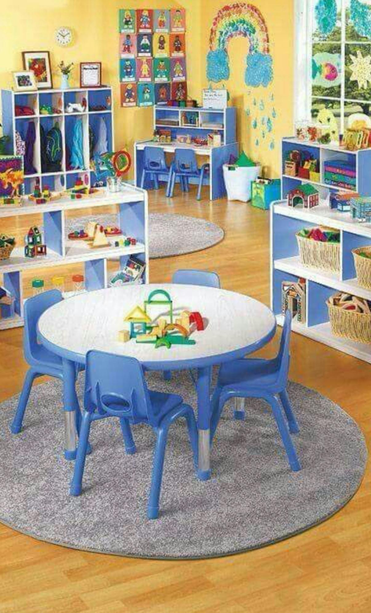 Classroom with small blue tables and chairs, shelves with toys and supplies