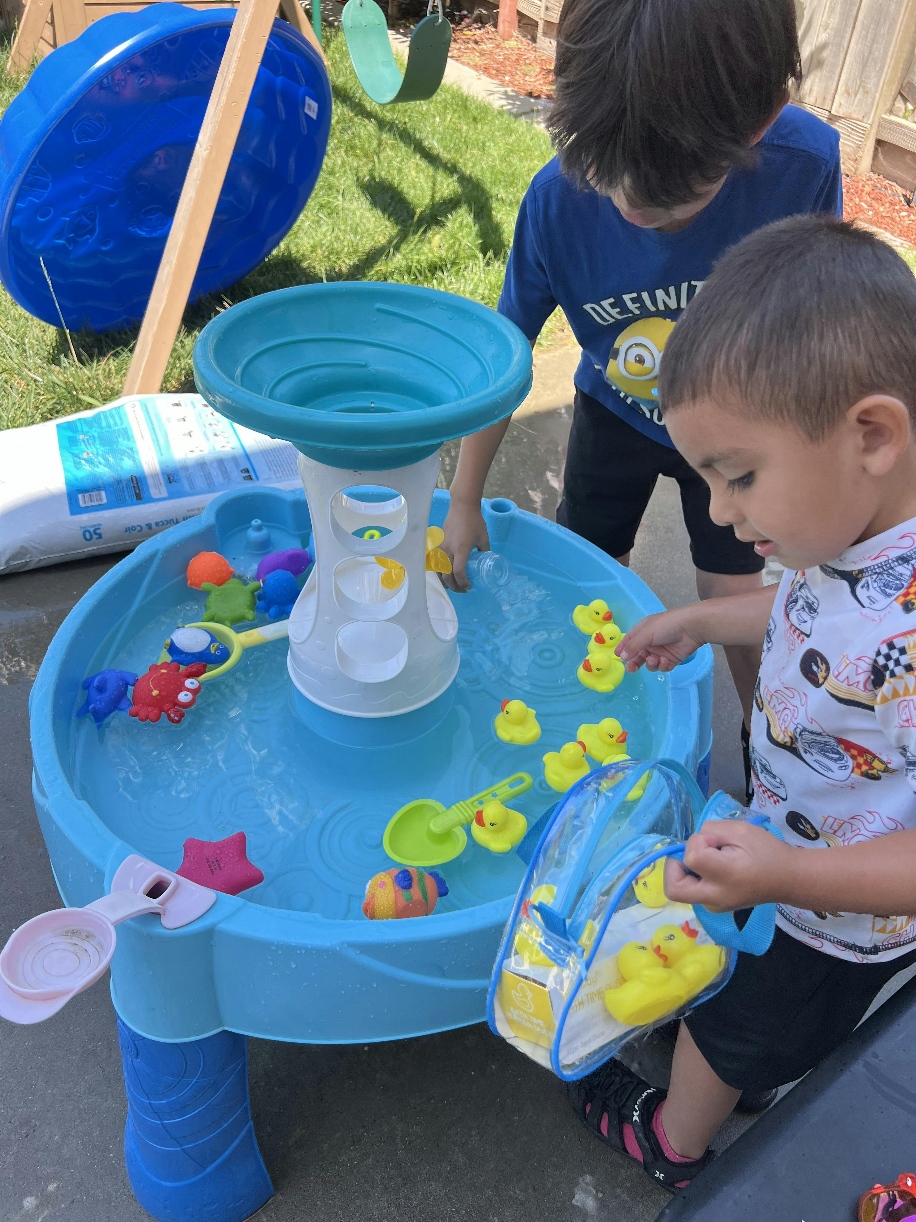 Two children playing with water and rubber ducks at an outdoor water table