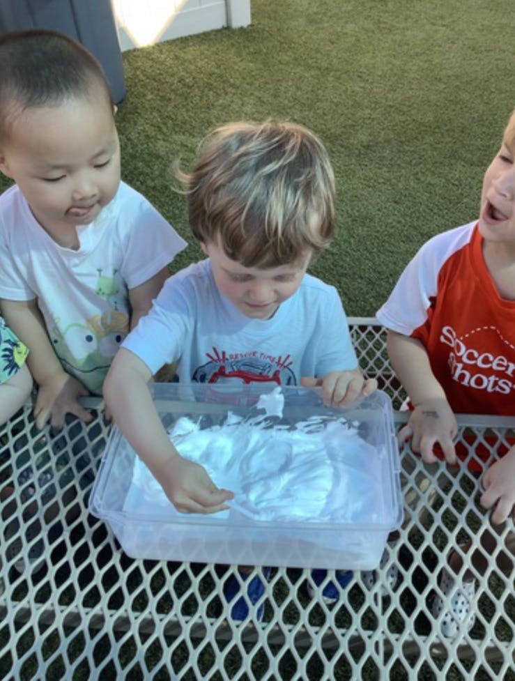 Three children playing with a container of white foam