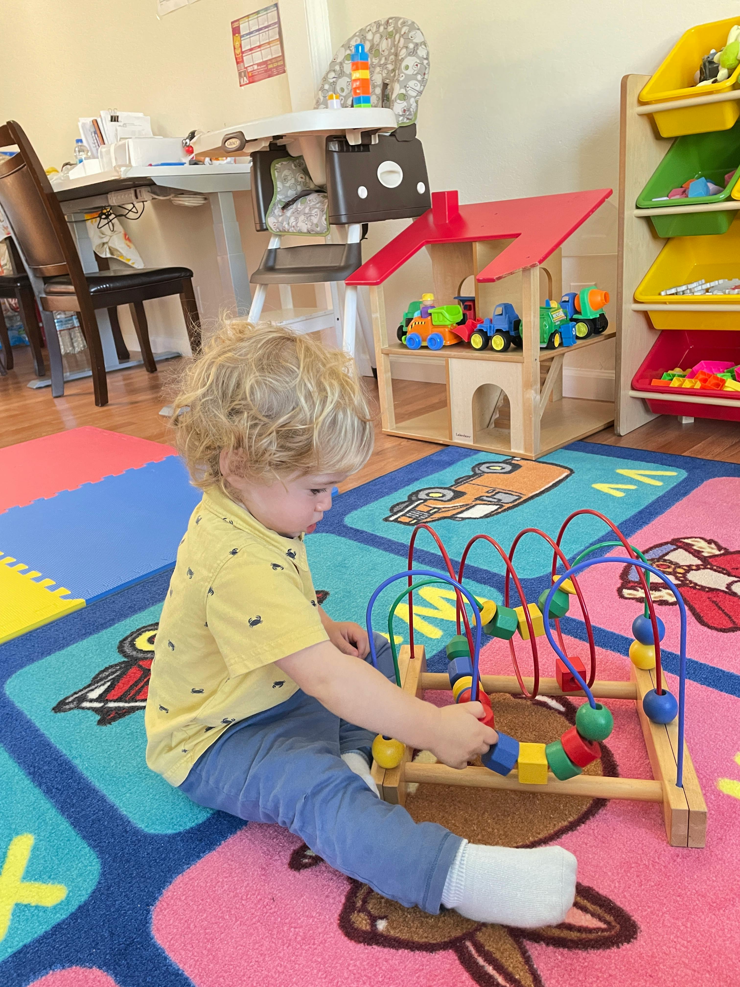 Child playing with a bead maze toy on a colorful rug