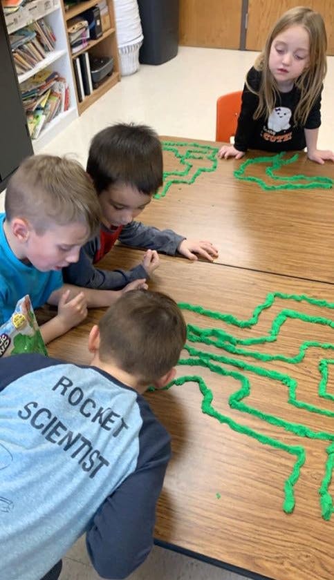 Children playing with green playdough on a table