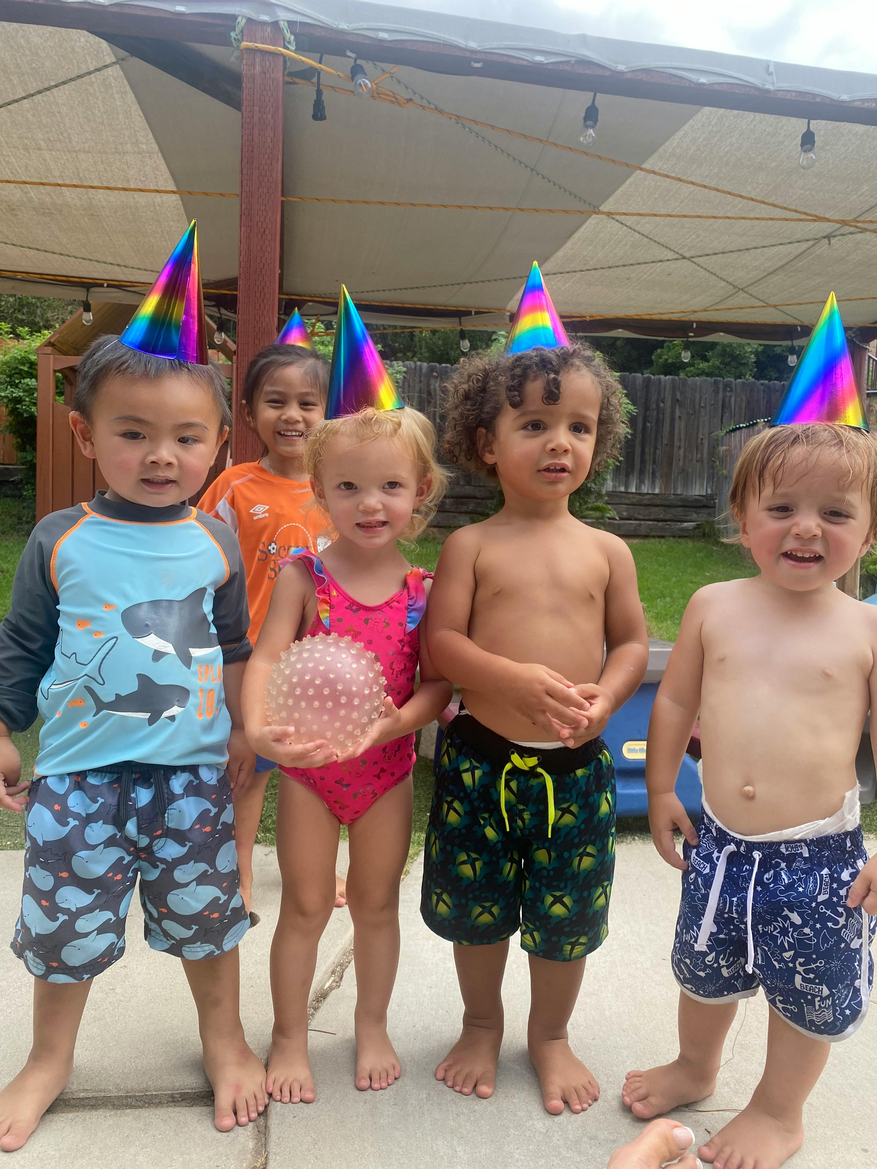 Group of children wearing rainbow party hats outdoors