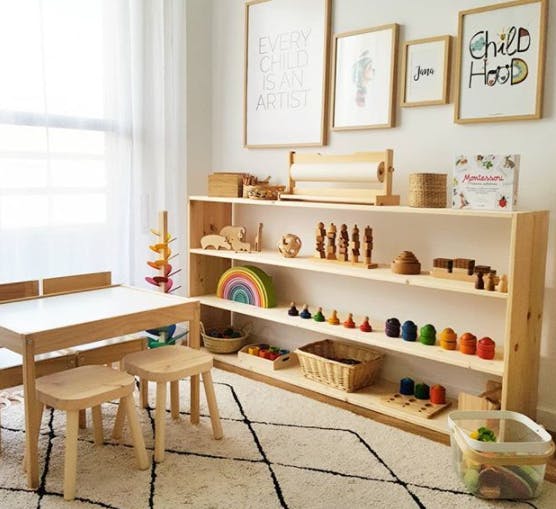 Children's play area with wooden table, stools, and shelves of toys