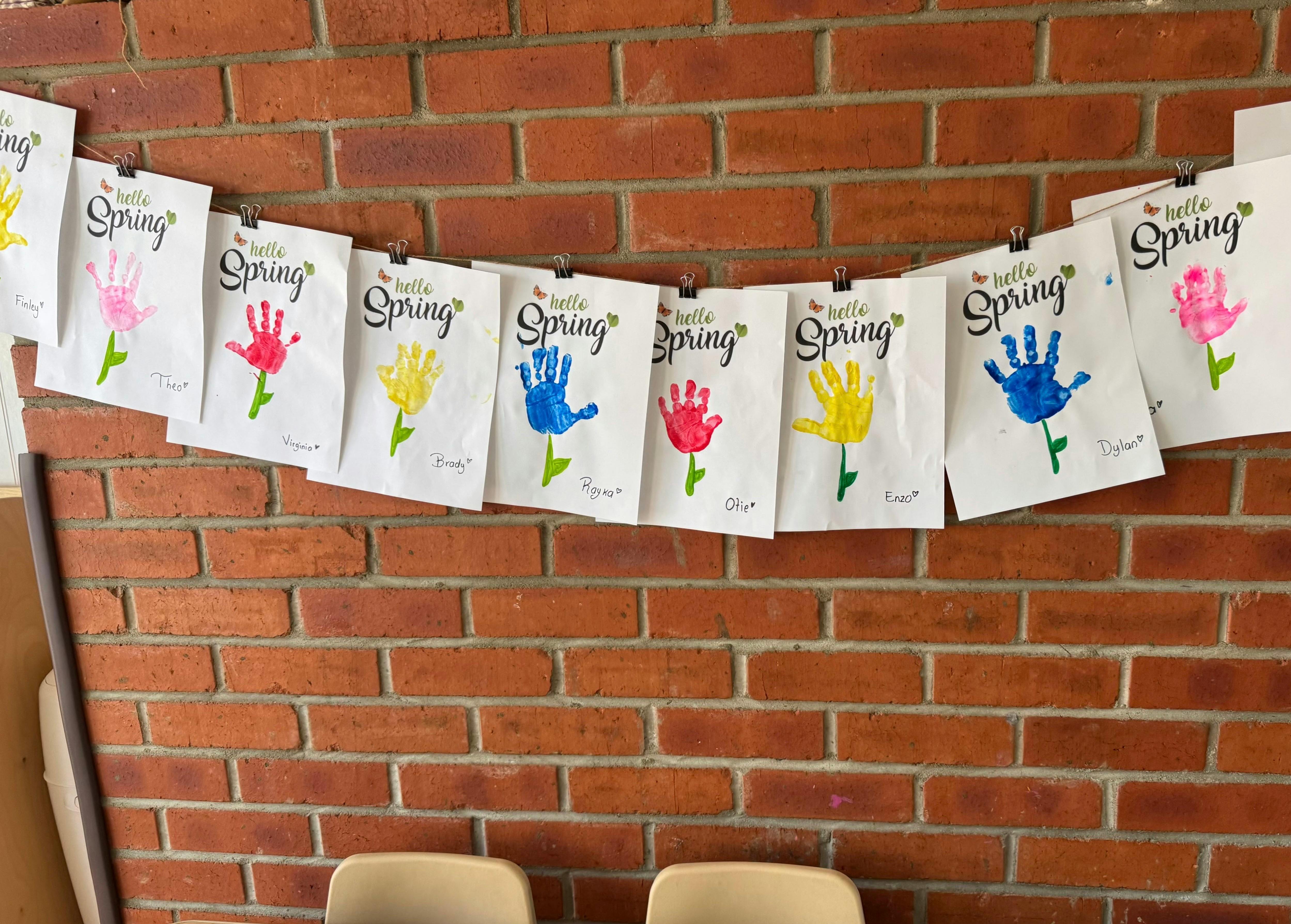 Children's handprint art with "Hello Spring" text on a brick wall