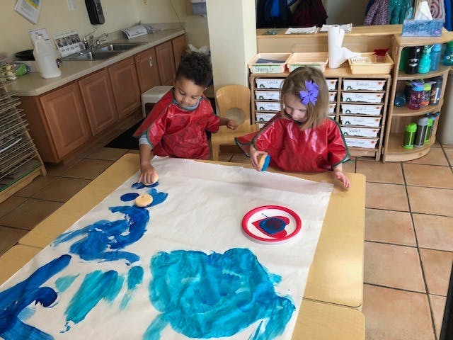 Two children in smocks painting on a large sheet of paper
