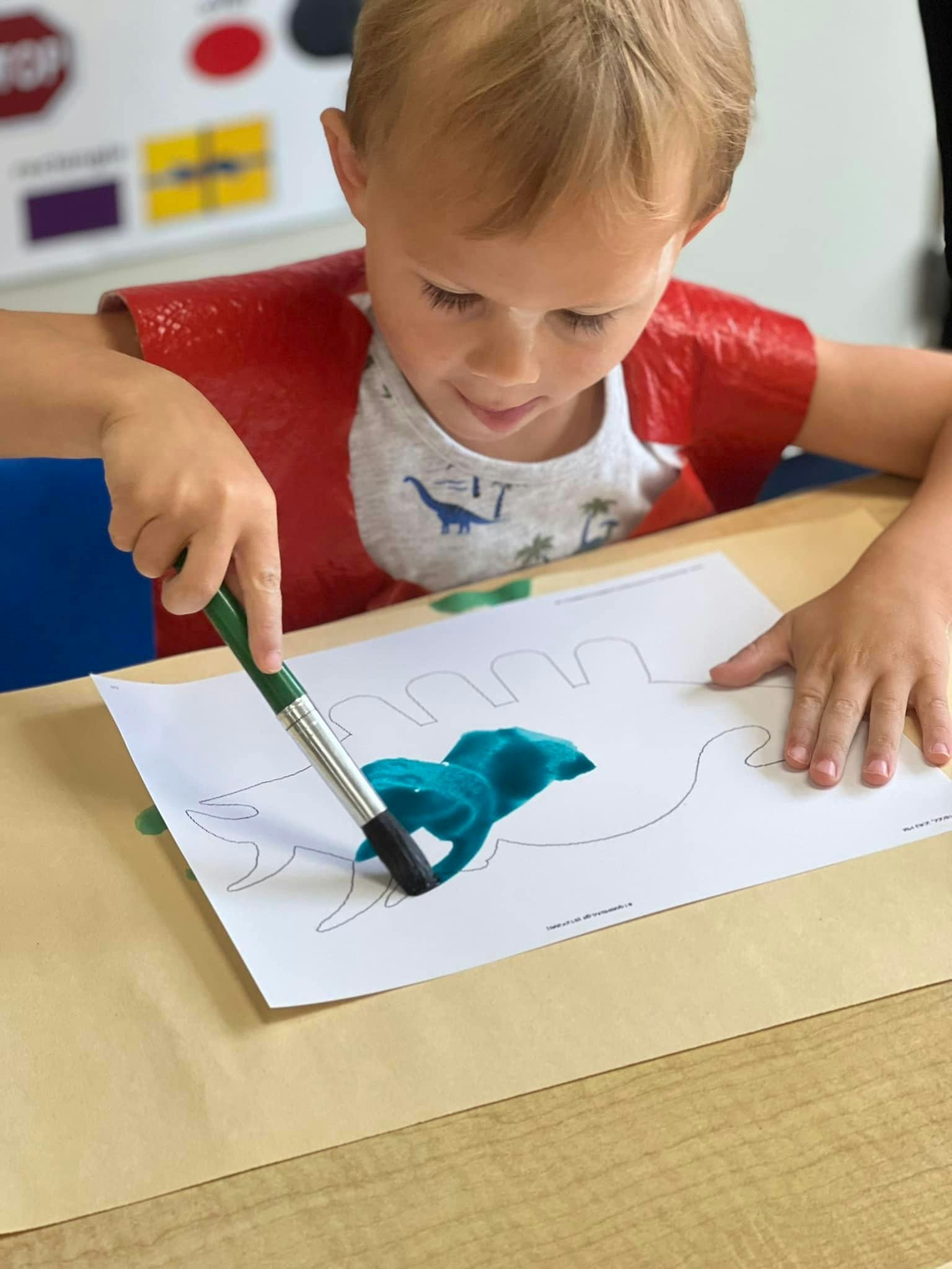 Child painting a dinosaur outline on paper
