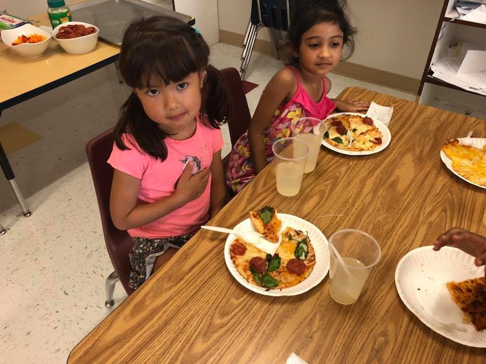 Two children sitting at a table with plates of pizza and drinks