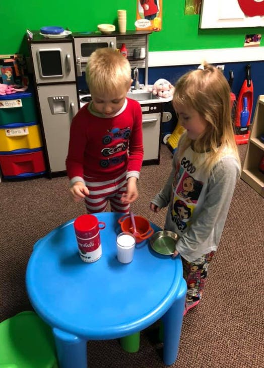 Two children playing with toy kitchen items at a small blue table
