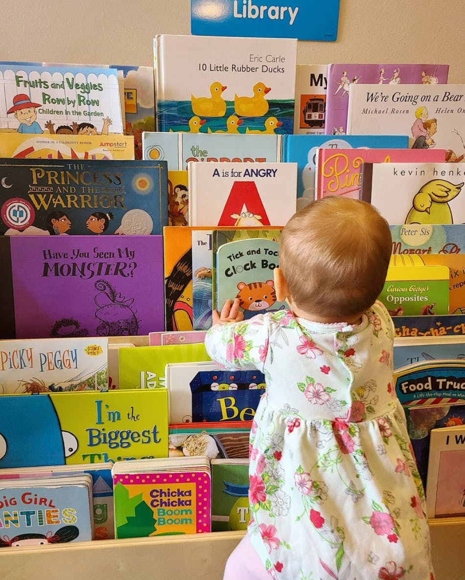 Child in a floral dress looking at books on a shelf in a library