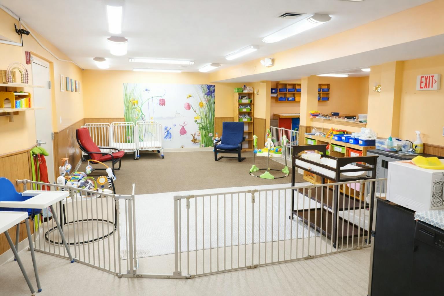 A colorful childcare room with cribs, playpens, chairs, and baby changing station