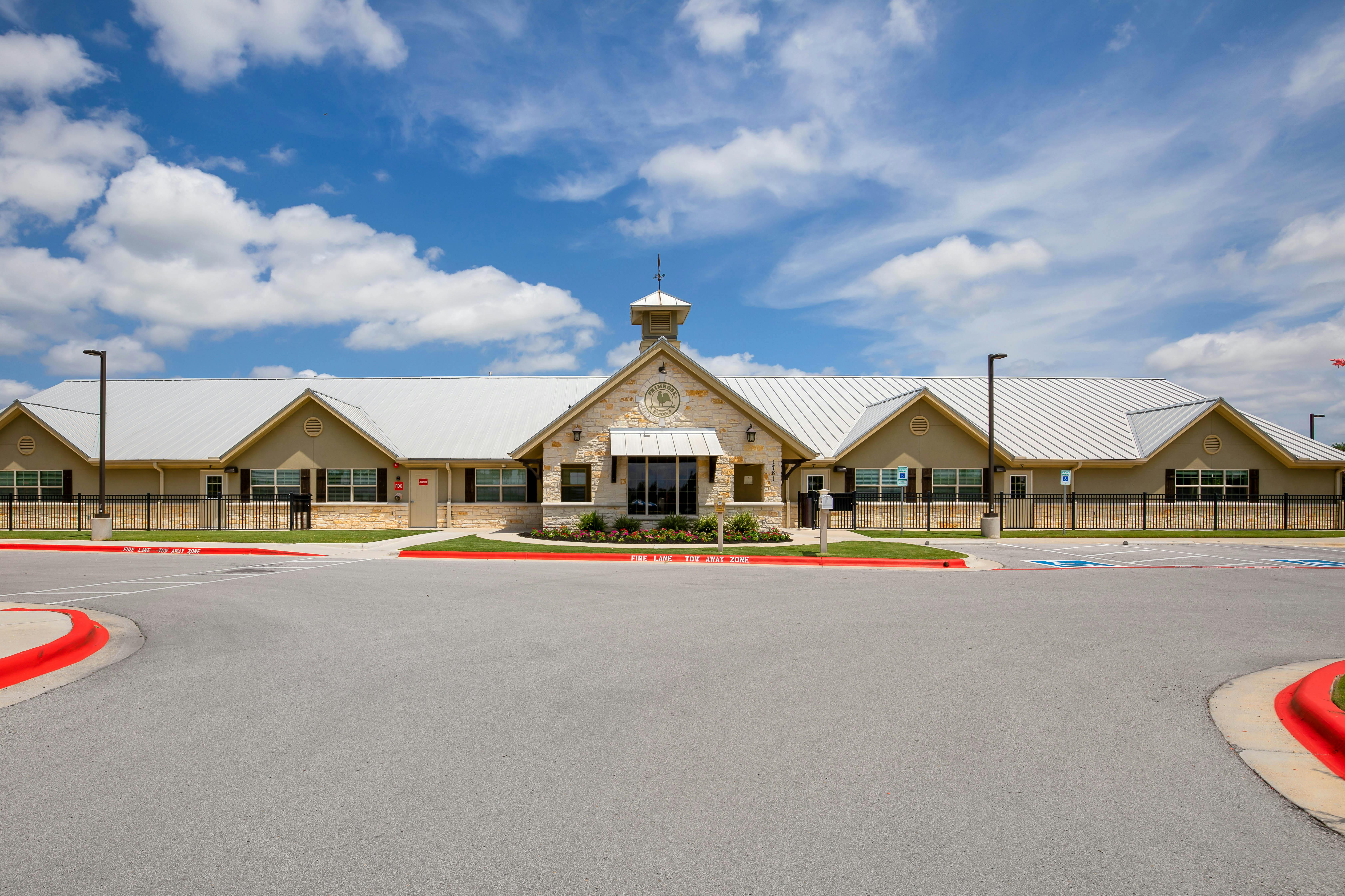 A beige building with a white metal roof, stone facade, and a sign that reads "Primrose Schools"