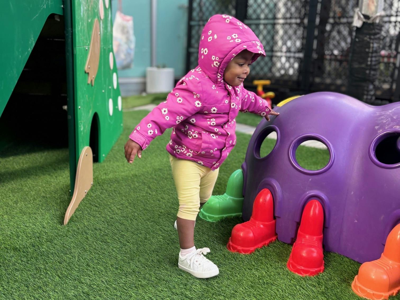 Child in a hooded jacket touching a purple play structure