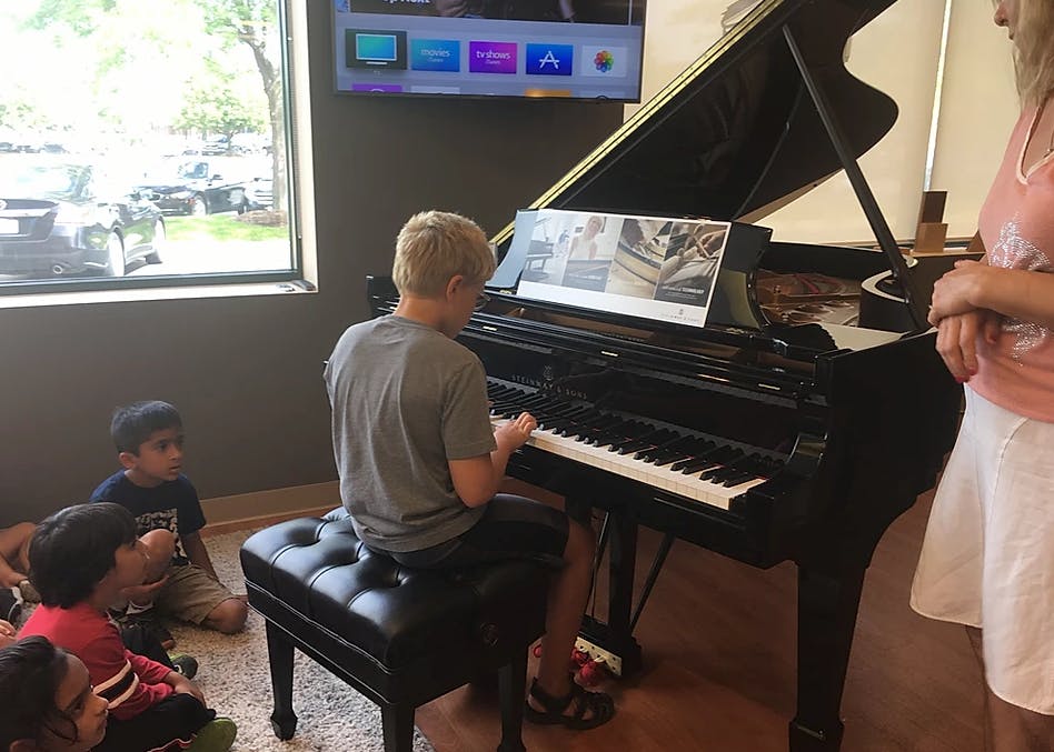 Teen playing a grand piano with children watching