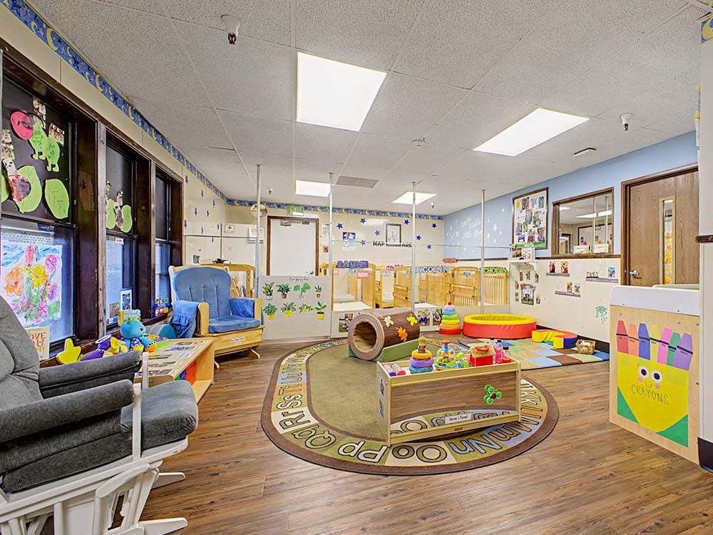 Childcare classroom with toys, cribs, a rocking chair, and an ABC rug