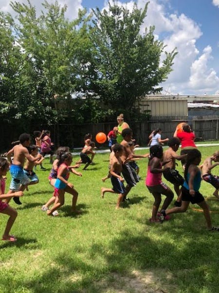 Many children running on grass with an orange ball