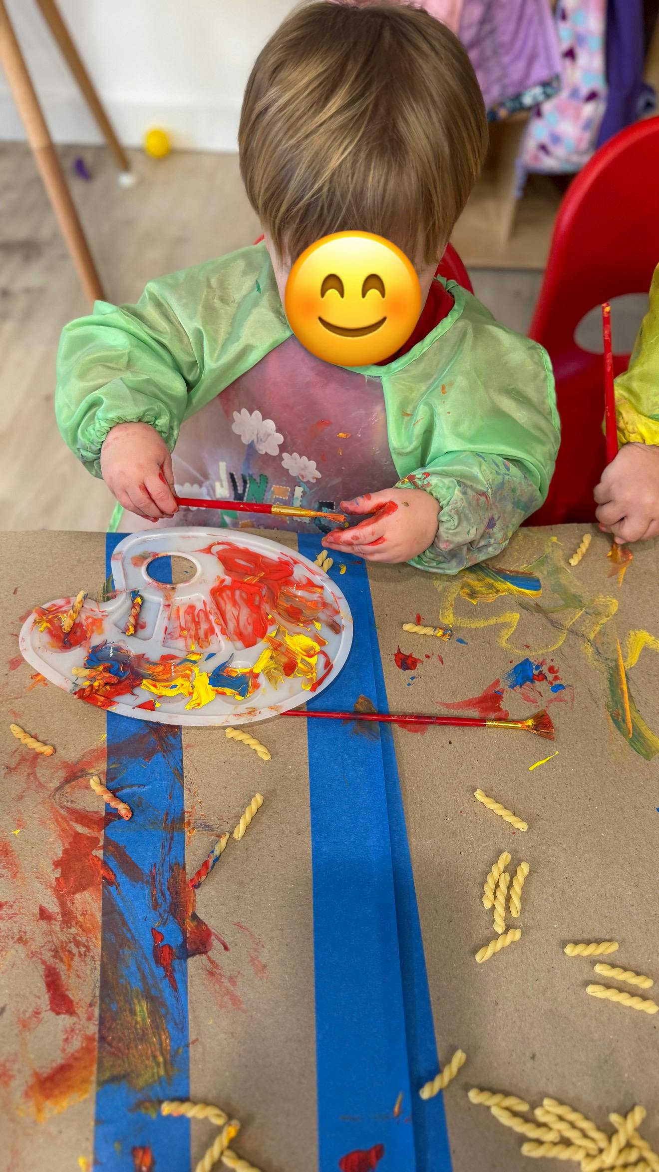 Child wearing a smock, painting with a paintbrush and palette
