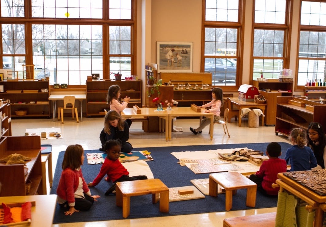 Children and an adult in a classroom with tables and rugs