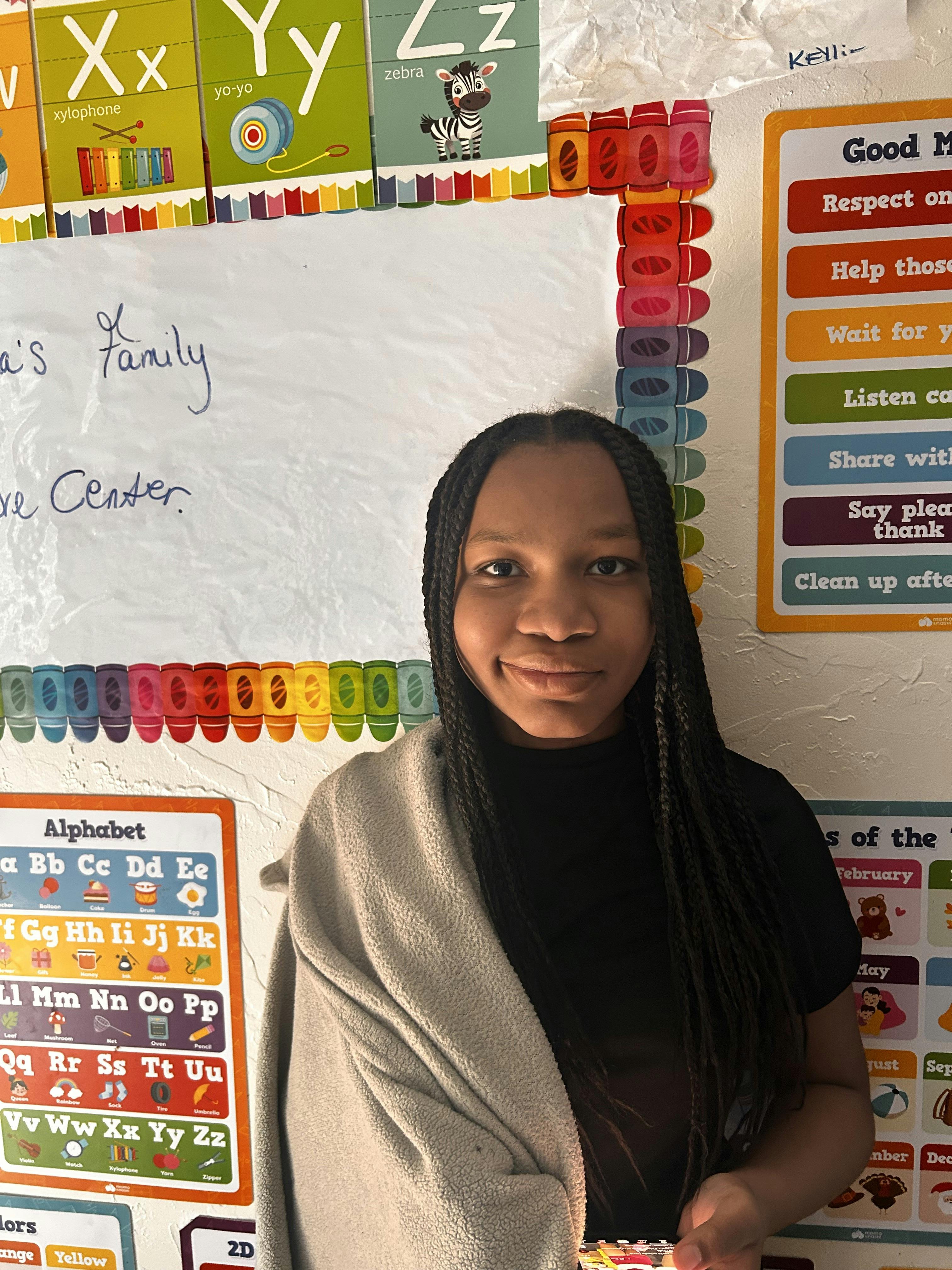 A teen with braided hair posing in a classroom with alphabet posters