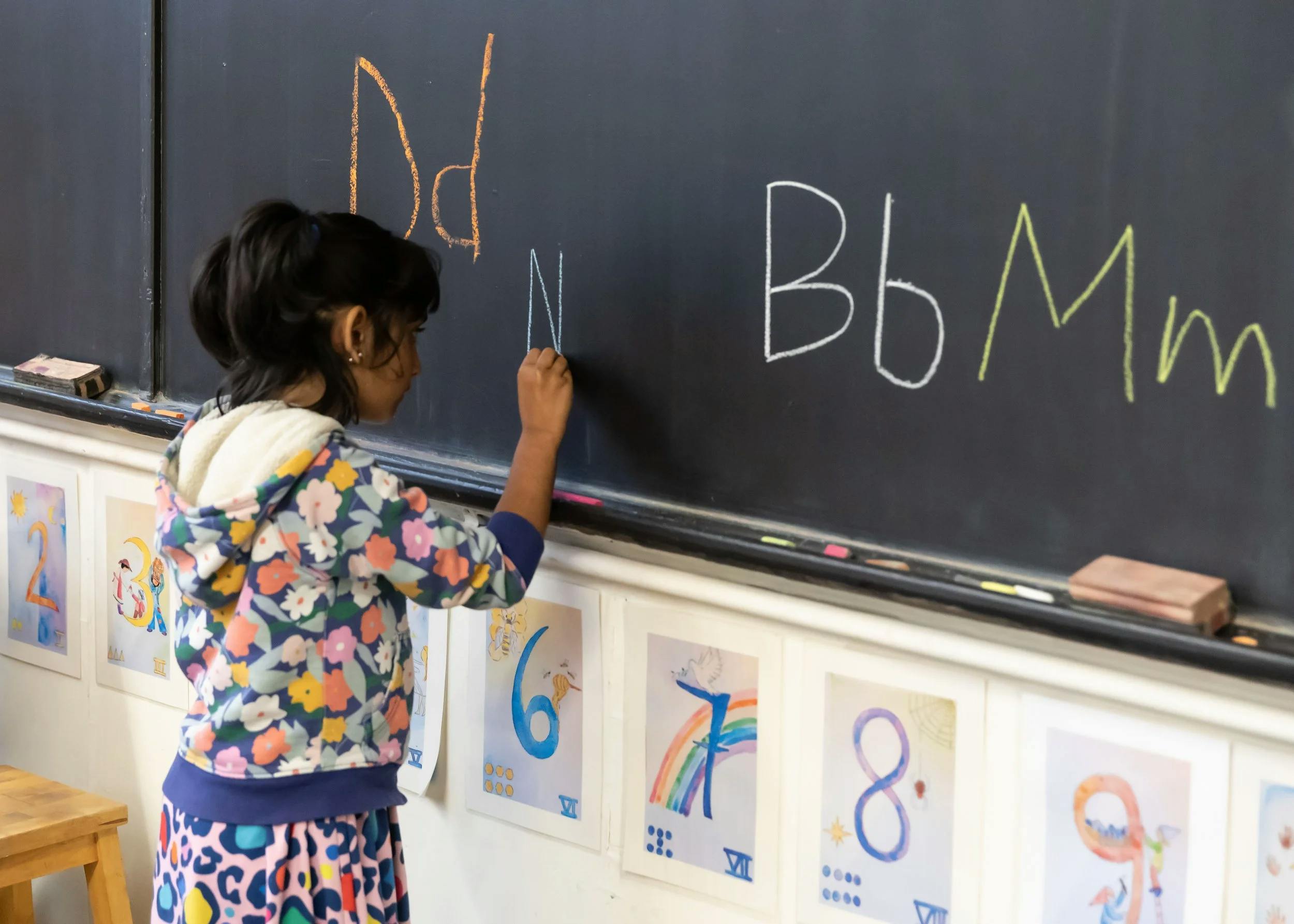 Child writing uppercase and lowercase 'N' on a blackboard in a classroom